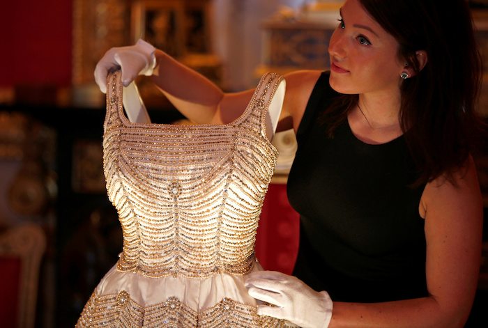 A member of staff of the Royal Collection poses with a dress worn by Britain's Queen Elizabeth, in the Crimson Drawing Room at Windsor Castle in Windsor, Britain September 15, 2016. The exhibition Fashioning a Reign: 90 Years of Style from The Queen's Wardrobe, will show at the castle from September 17, 2016 to January 8, 2017.  REUTERS/Peter Nicholls 