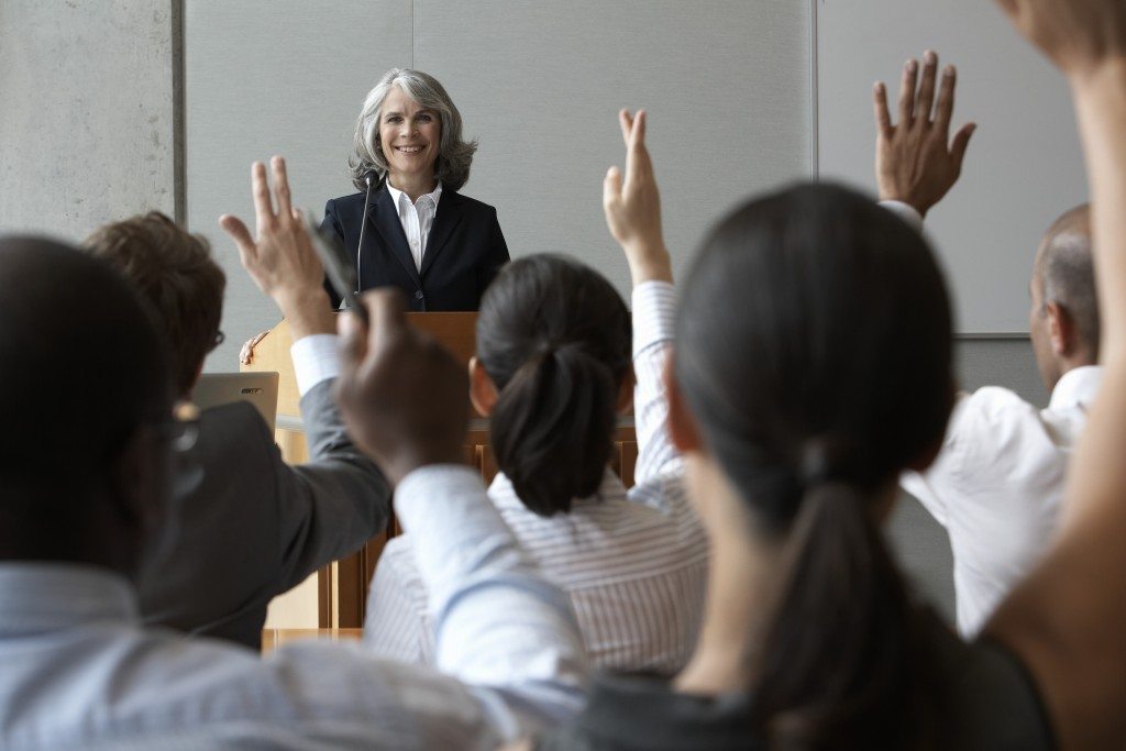 Businesswoman at podium with colleauges raising their hands, smiling